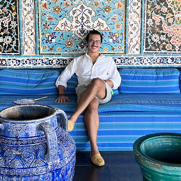 A designer seated on a blue striped sofa, surrounded by intricate mosaic tiles and pottery, reflecting creativity and culture.