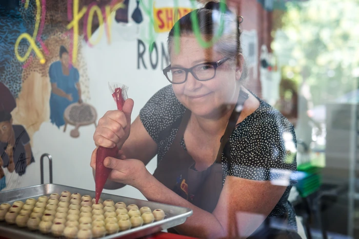A woman in an apron decorates chocolates with a piping bag behind a glass window at Roni-Sue's Chocolates in NYC.