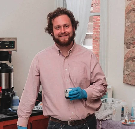 Ryley, a ceramic artist and kintsugi expert, smiles while holding a cup in a bright studio setting.