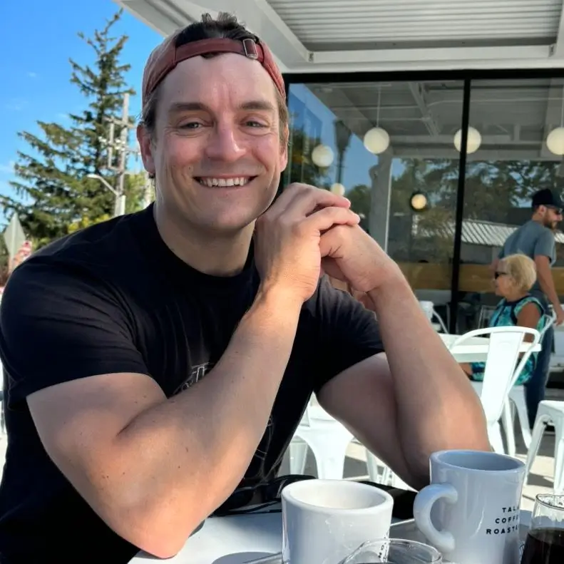 Smiling host at a café, ready to share latte art skills, surrounded by coffee cups and a sunny atmosphere.
