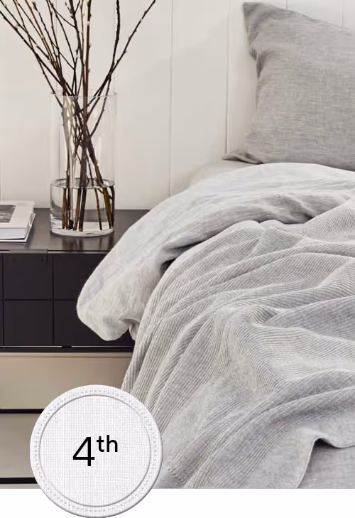 Bed with grey sheets and bedside table with white wall