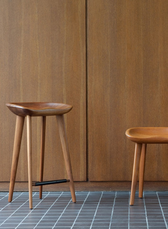 Two BassamFellows Tractor Stools in solid wood against a timber-panelled wall