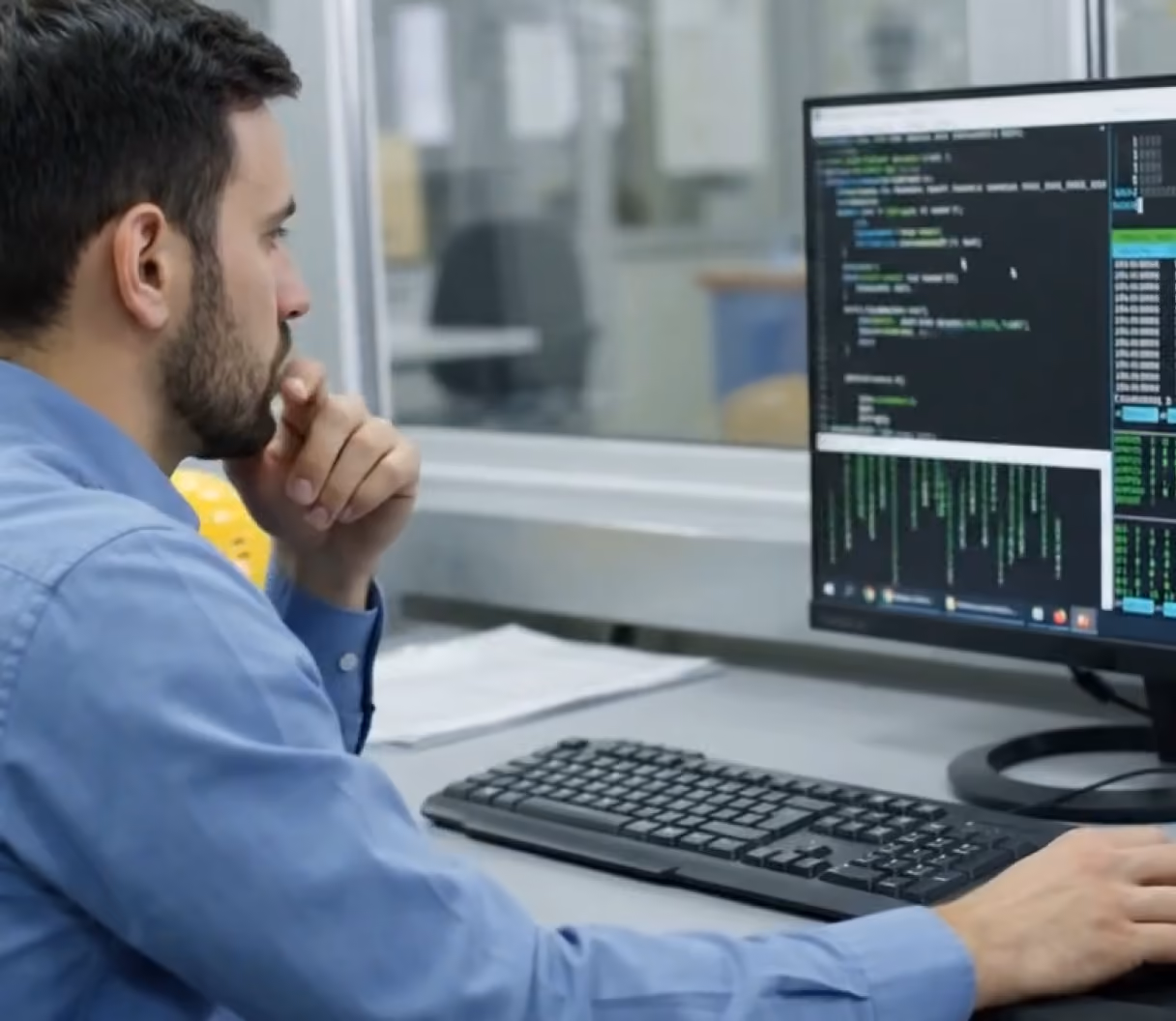 Developer working at a computer station with two monitors and headphones nearby.