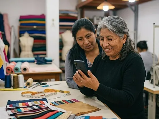 Two women in a fabric workshop looking at a smartphone, surrounded by colorful textiles and sewing tools.