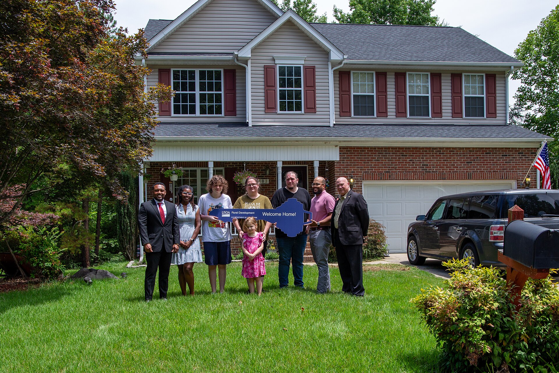 New homeowners holding a Welcome Home key in front of a USDA Rural Development financed house