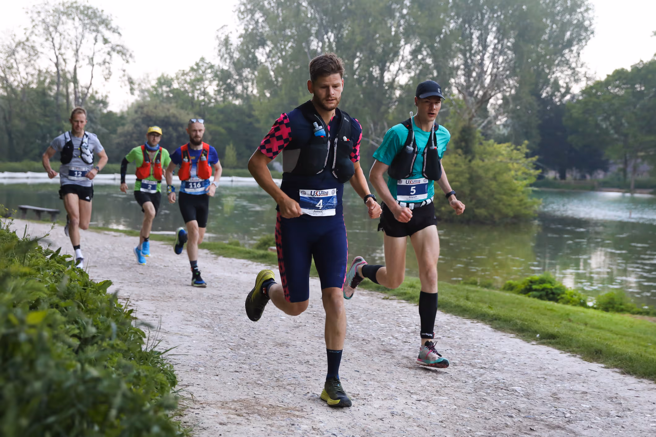 A group of runners running along a paved path by a lake