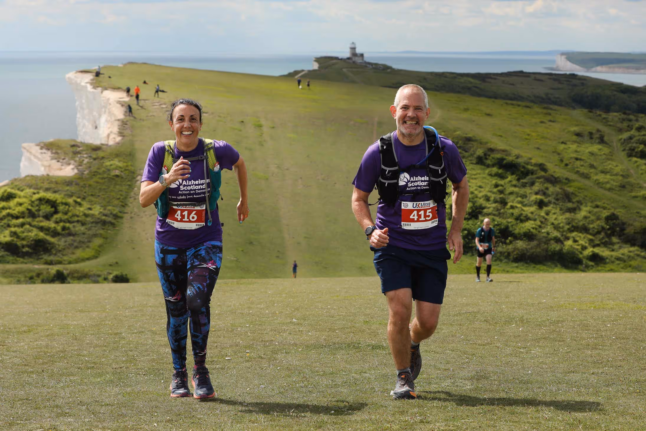 Two runners smiling at the camera with a backdrop of Birling Gap, Eastbourne