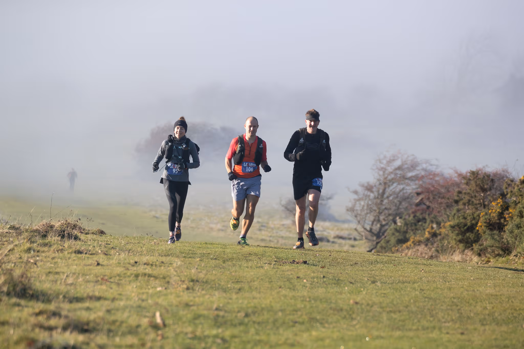 Three people are running on a grassy field during a foggy day.