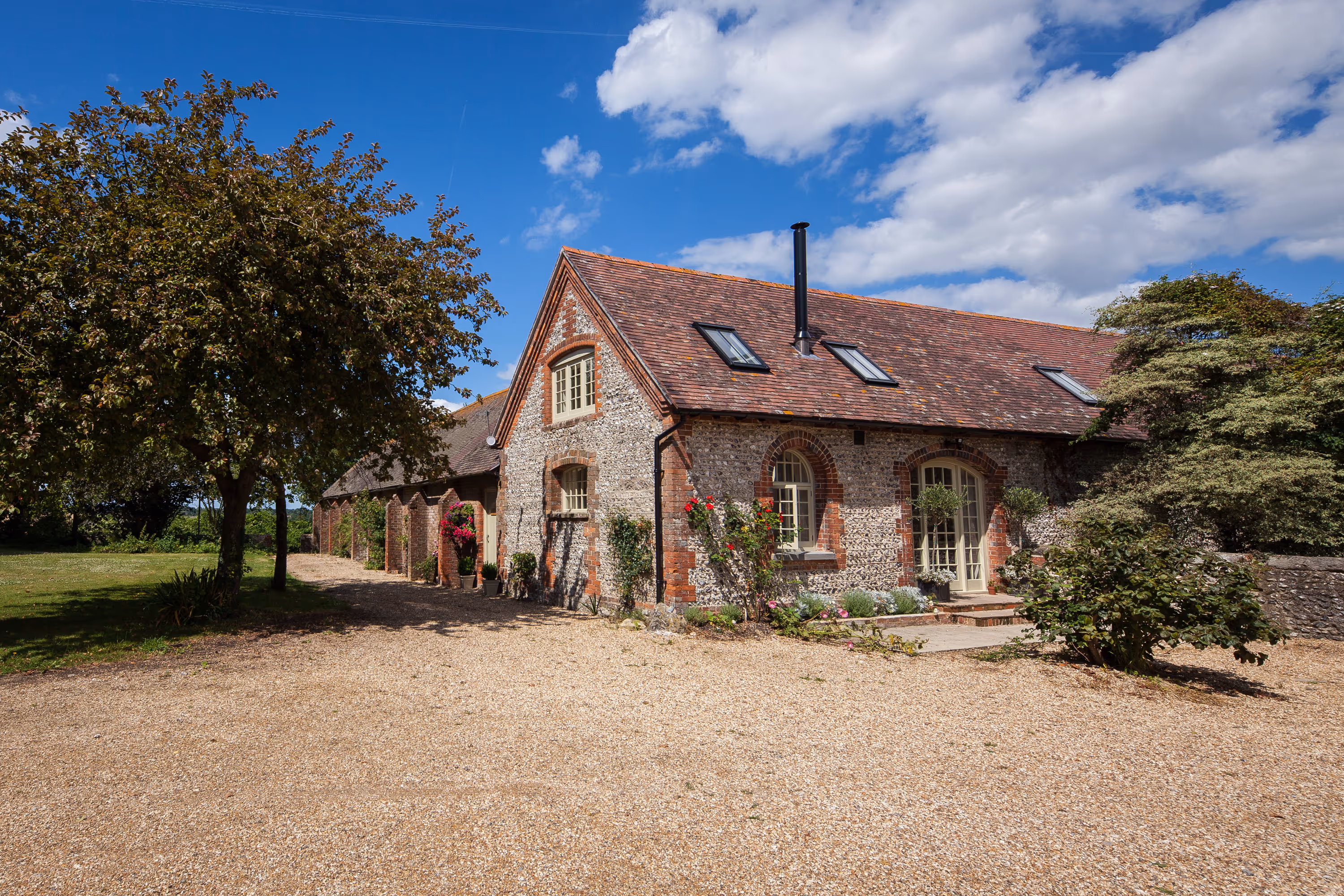 A red-brick house with a stone pathway, surrounded by trees, under a partly cloudy sky.