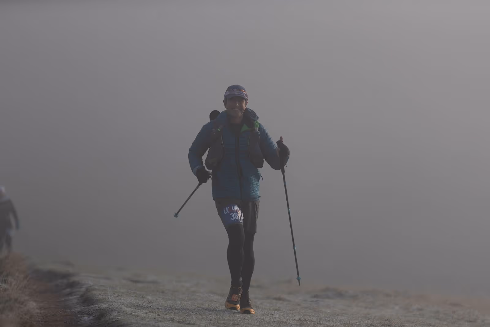 A person is hiking with trekking poles on a foggy trail.