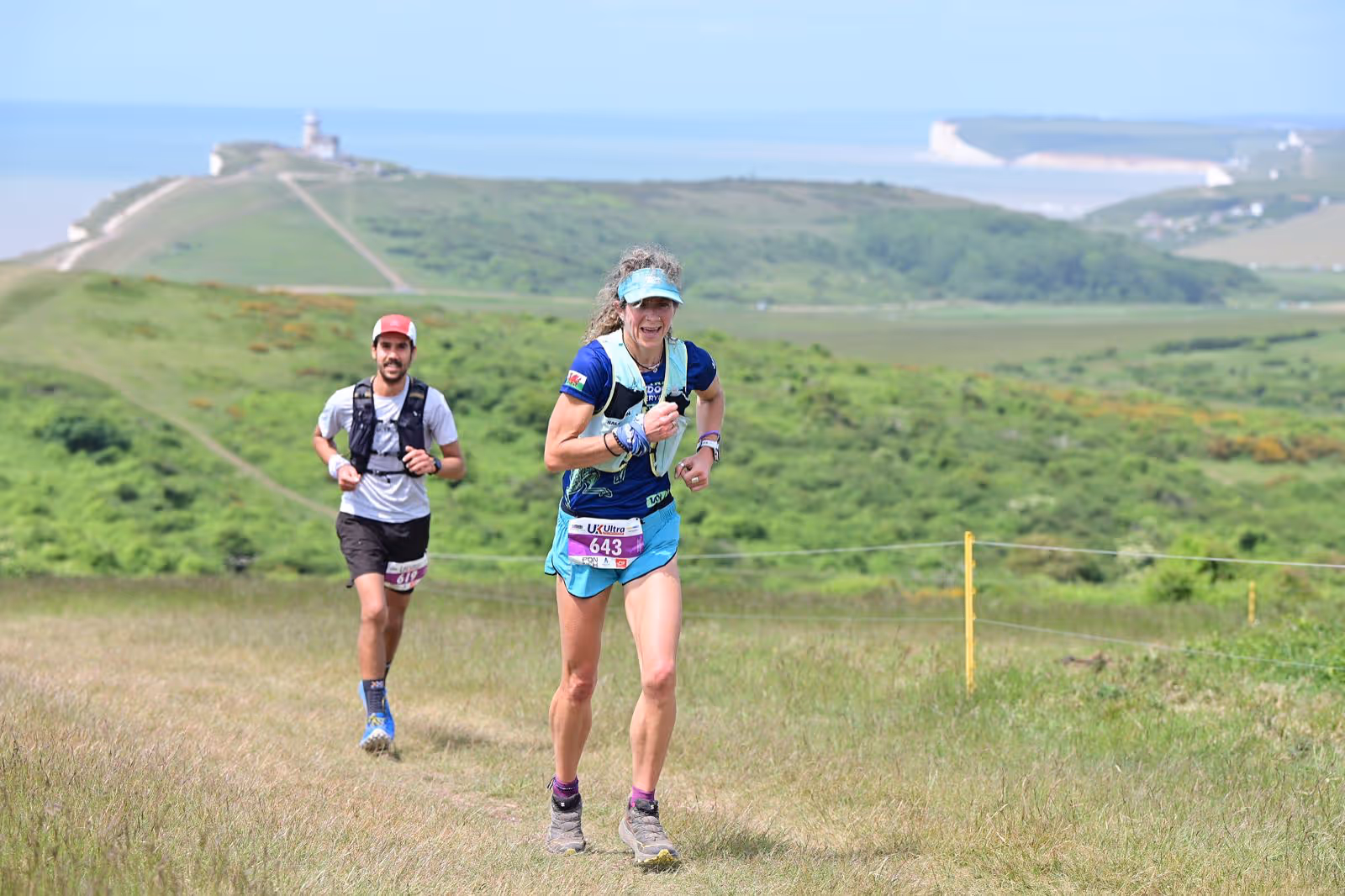 Two runners in a race, with a scenic coastline in the background.