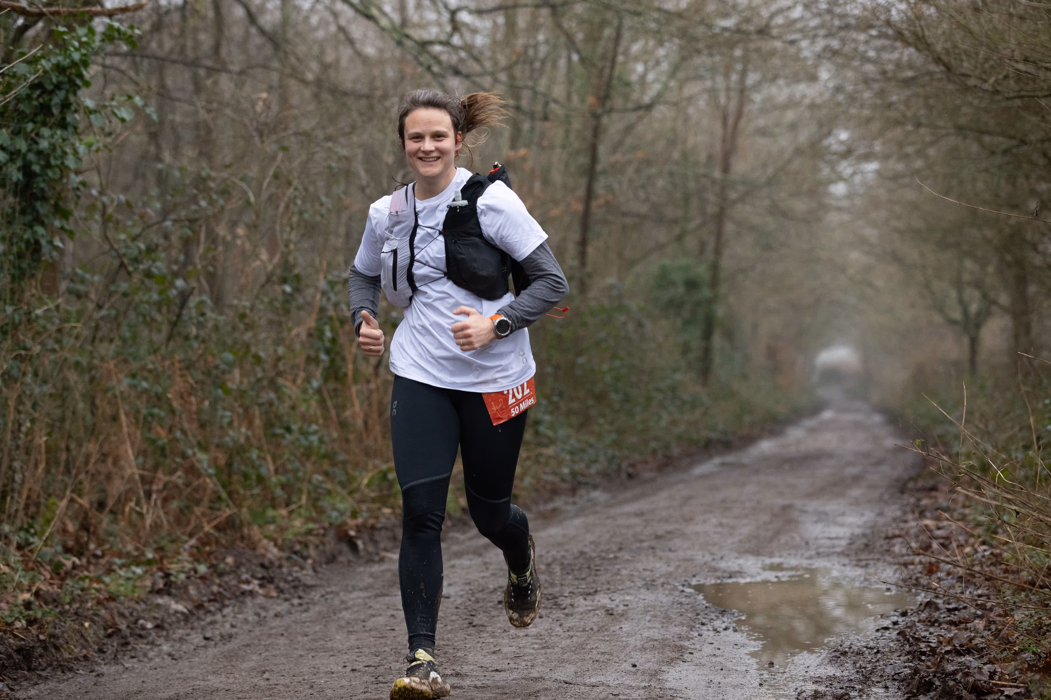 A person wearing running gear jogs on a muddy forest trail.