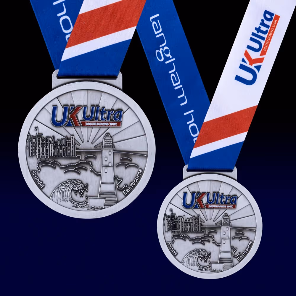Two UK Ultra marathon medals with lighthouse design and blue, red, and white ribbons.