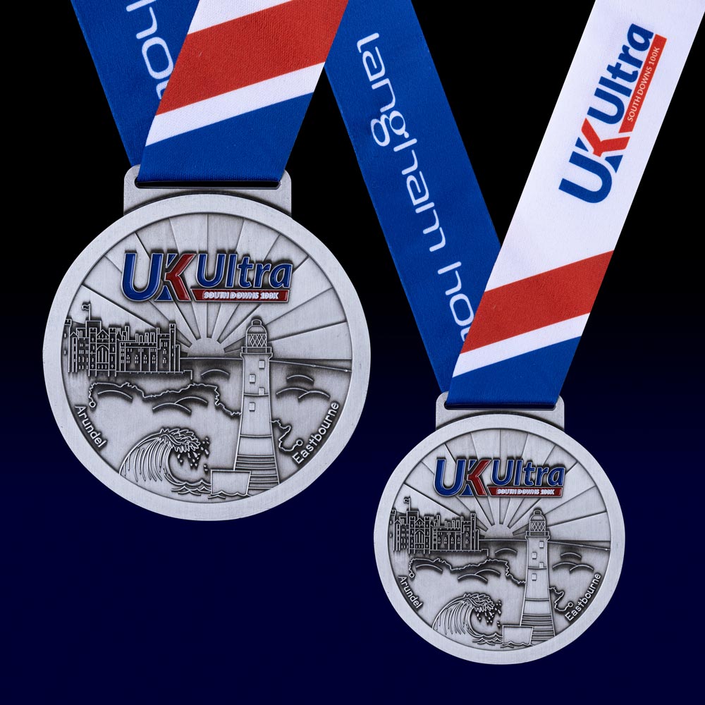 Two UK Ultra marathon medals with lighthouse design and blue, red, and white ribbons.