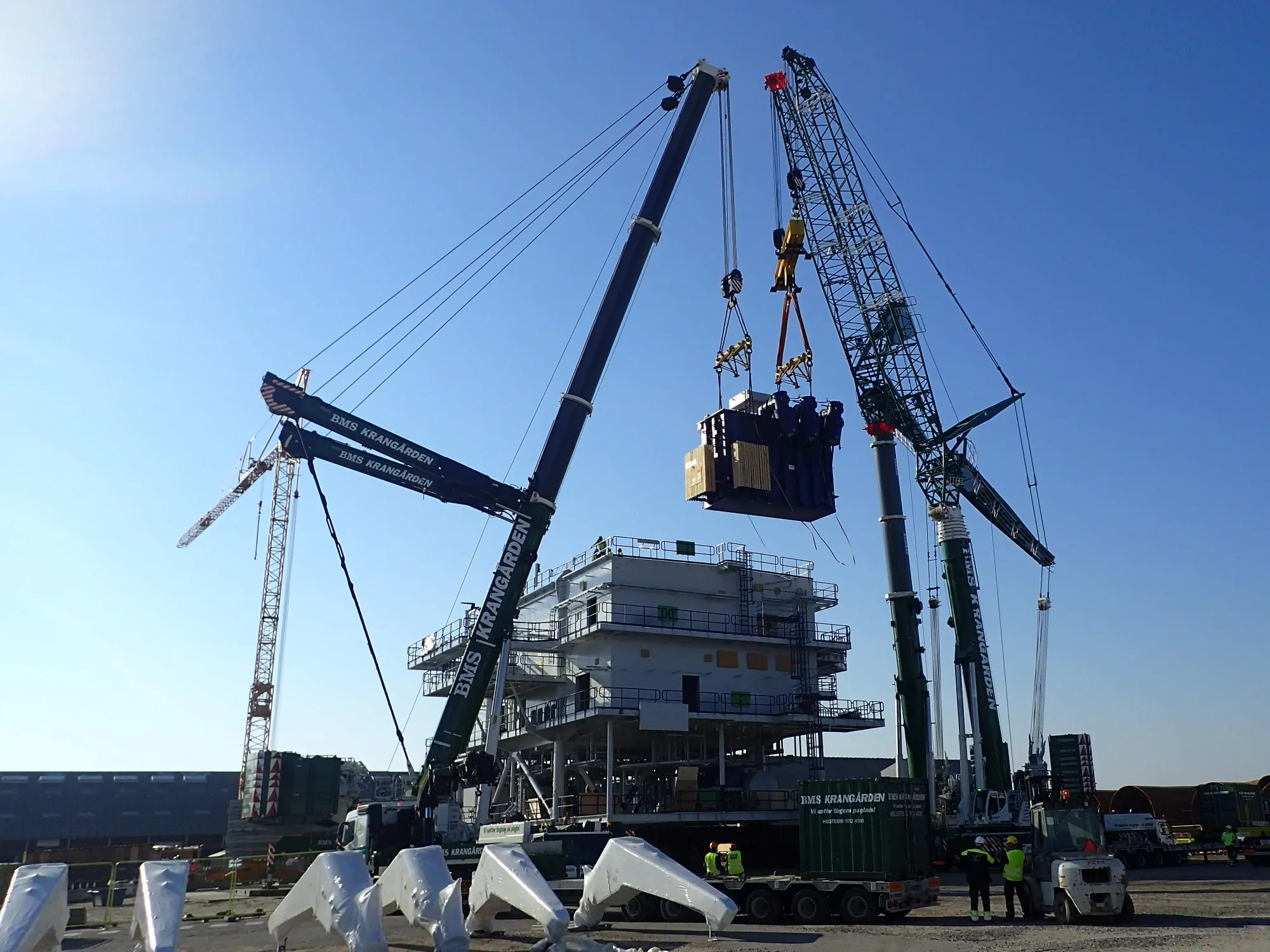 Power transformer being lifted by crane onto an offshore substation topside at the quayside
