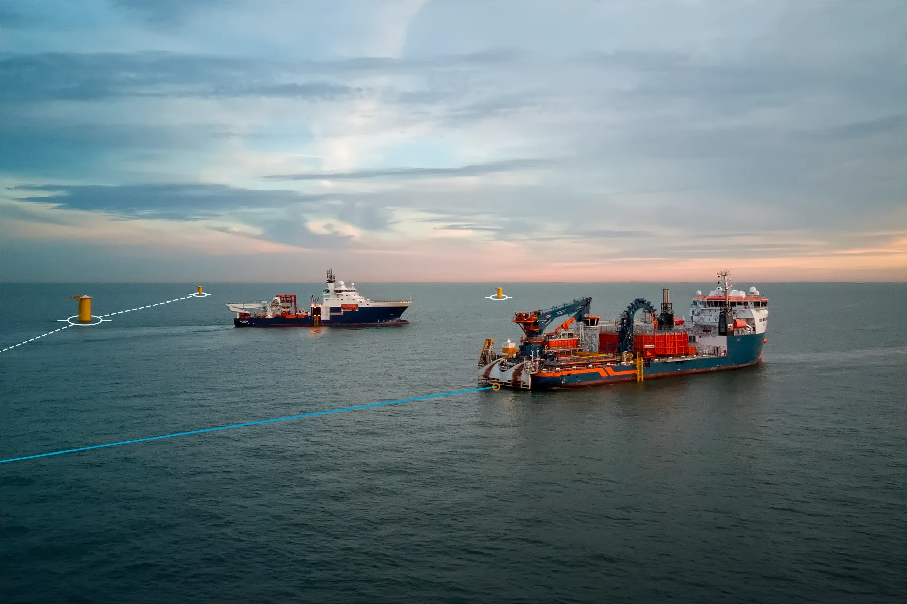Cable-laying vessel at dusk in an offshore wind farm under construction, with blue and white lines marking the cable route from its stern to the yellow monopile foundations.