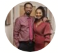 Smiling man and woman standing close together indoors, dressed in coordinated red outfits.