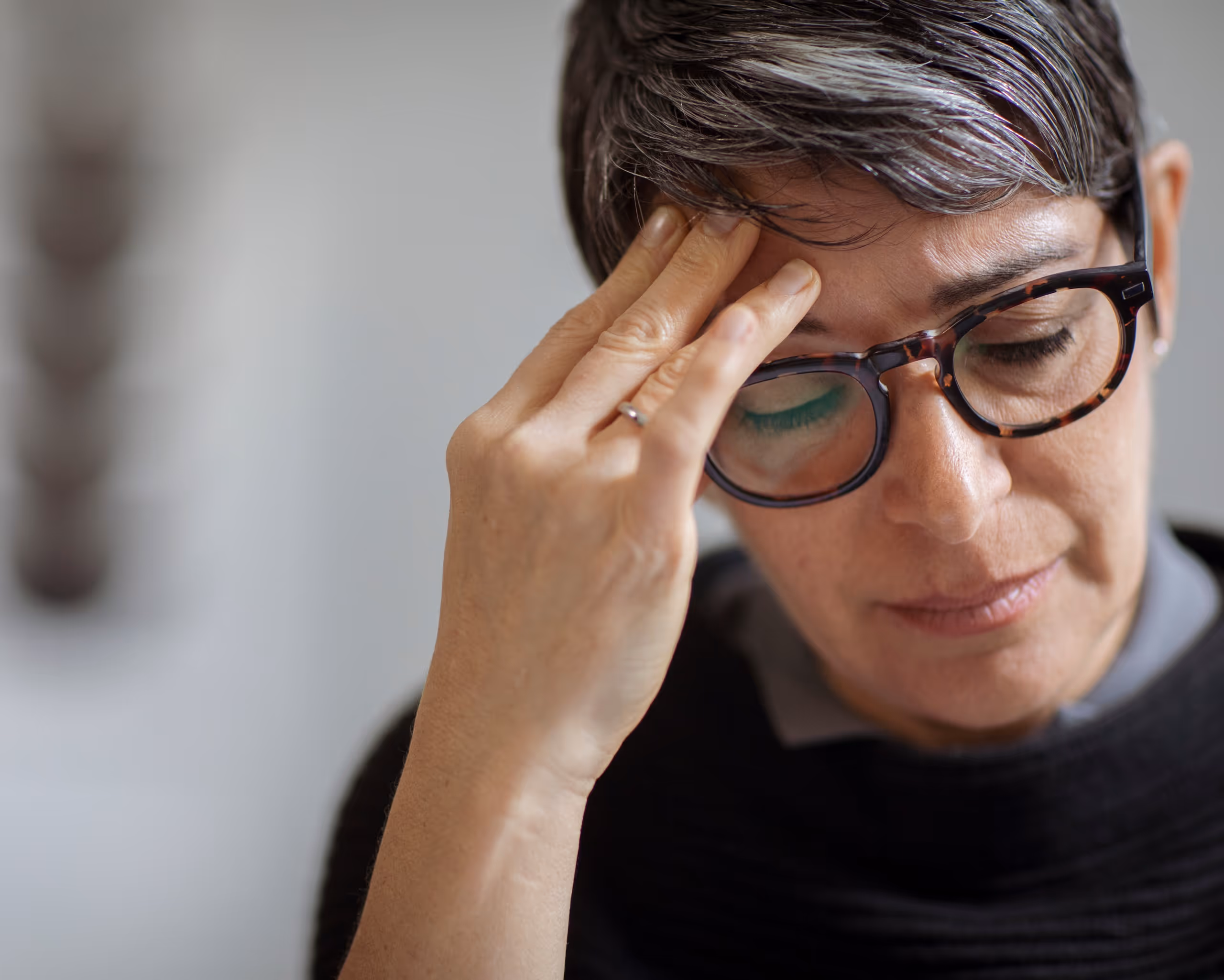 A woman wearing glasses holds her head with her hands