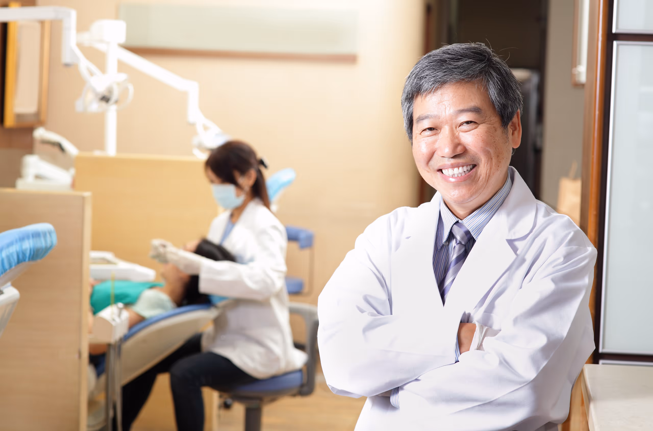 Smiling dentist in white coat standing in dental office with assistant