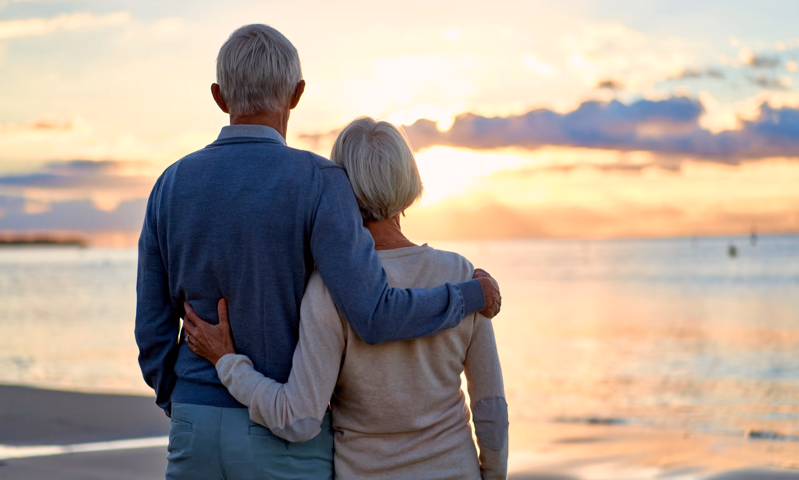 Elderly couple embracing, watching sunset together on peaceful beach