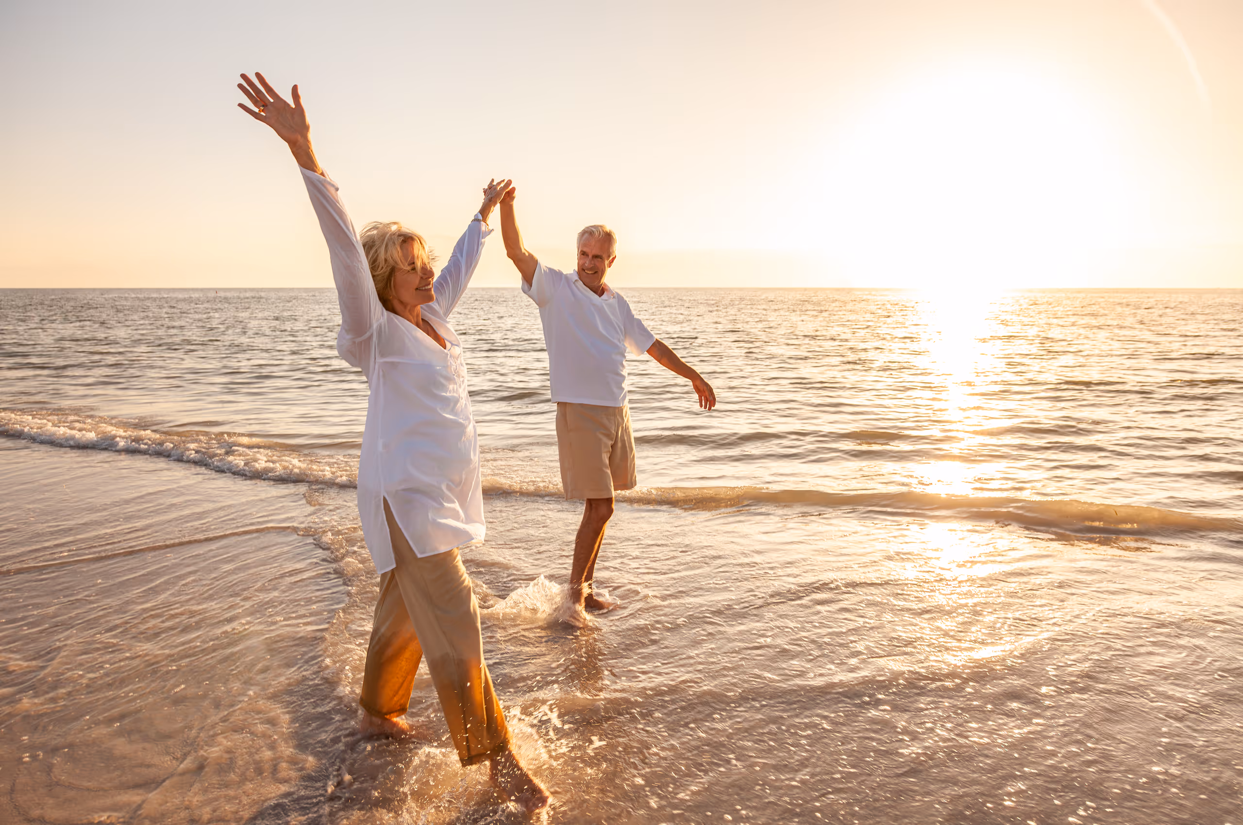 Joyful couple dancing in ocean waves at golden sunset