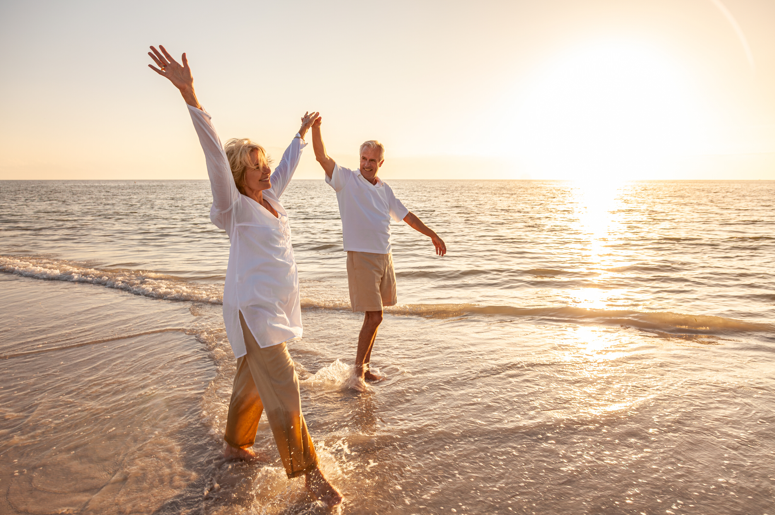 Joyful couple dancing in ocean waves at golden sunset