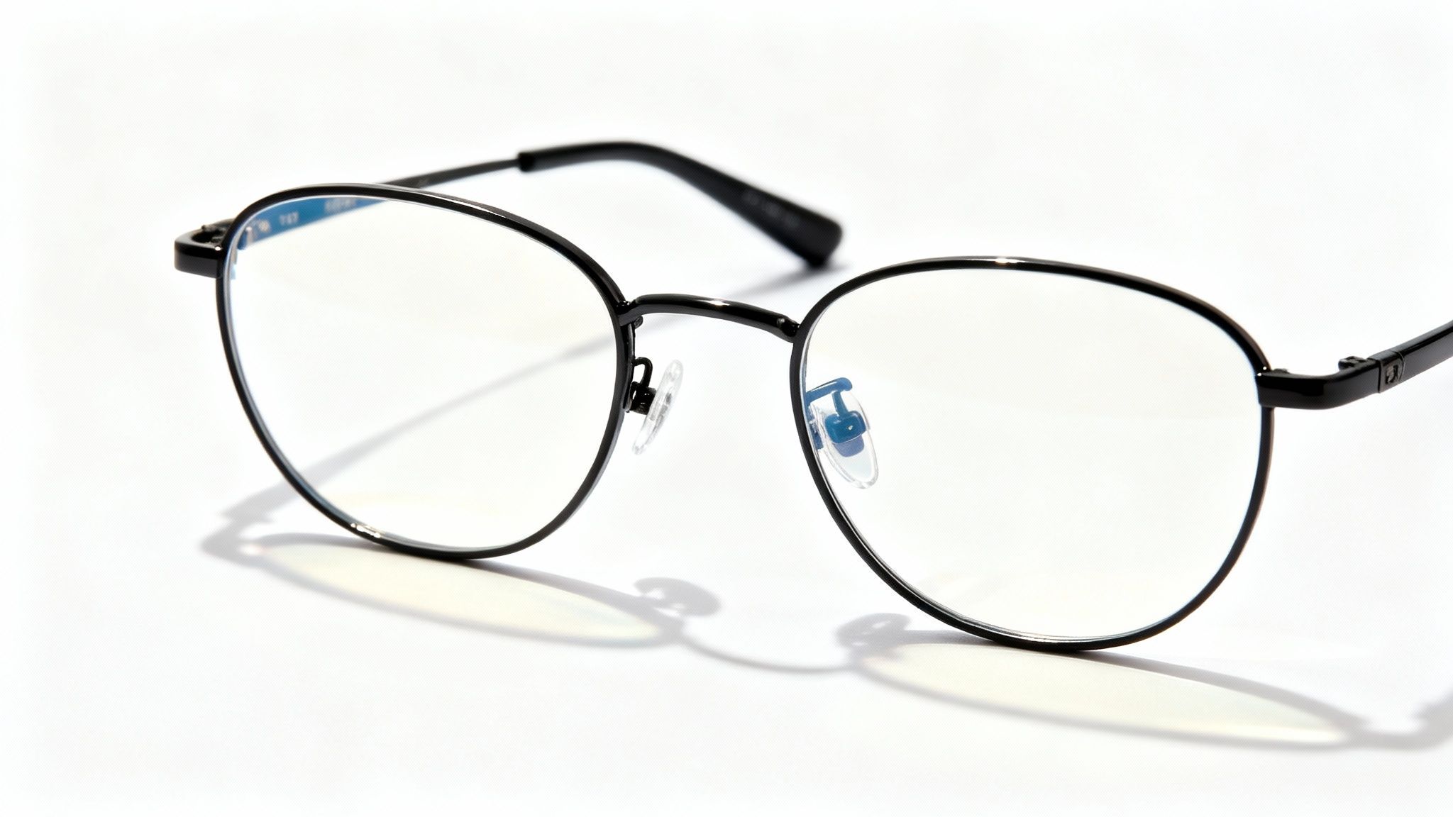Black round metal frame eyeglasses with clear lenses casting shadow on white surface