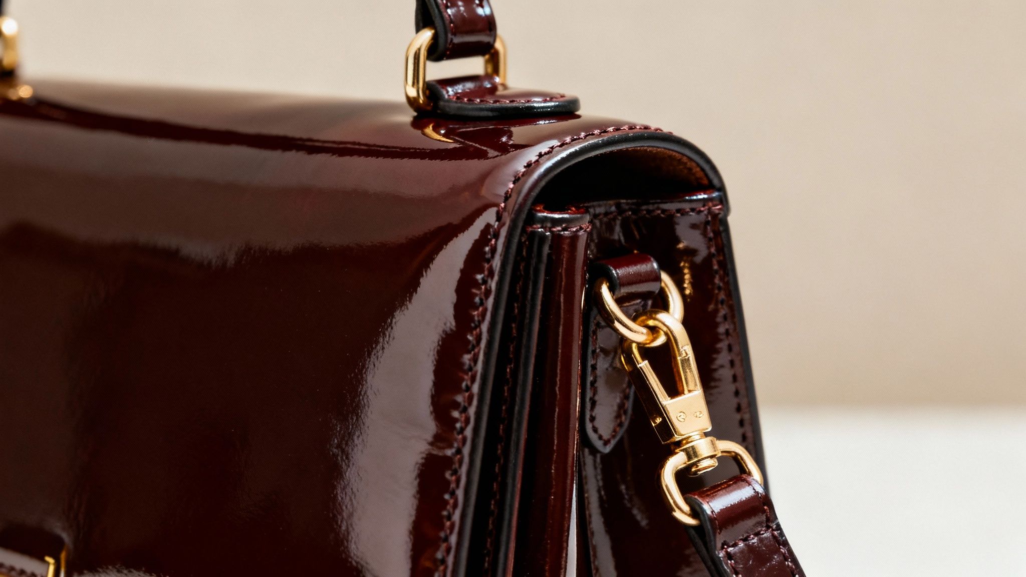 Luxury burgundy patent patent leather handbag with gold hardware and glossy reflective surface