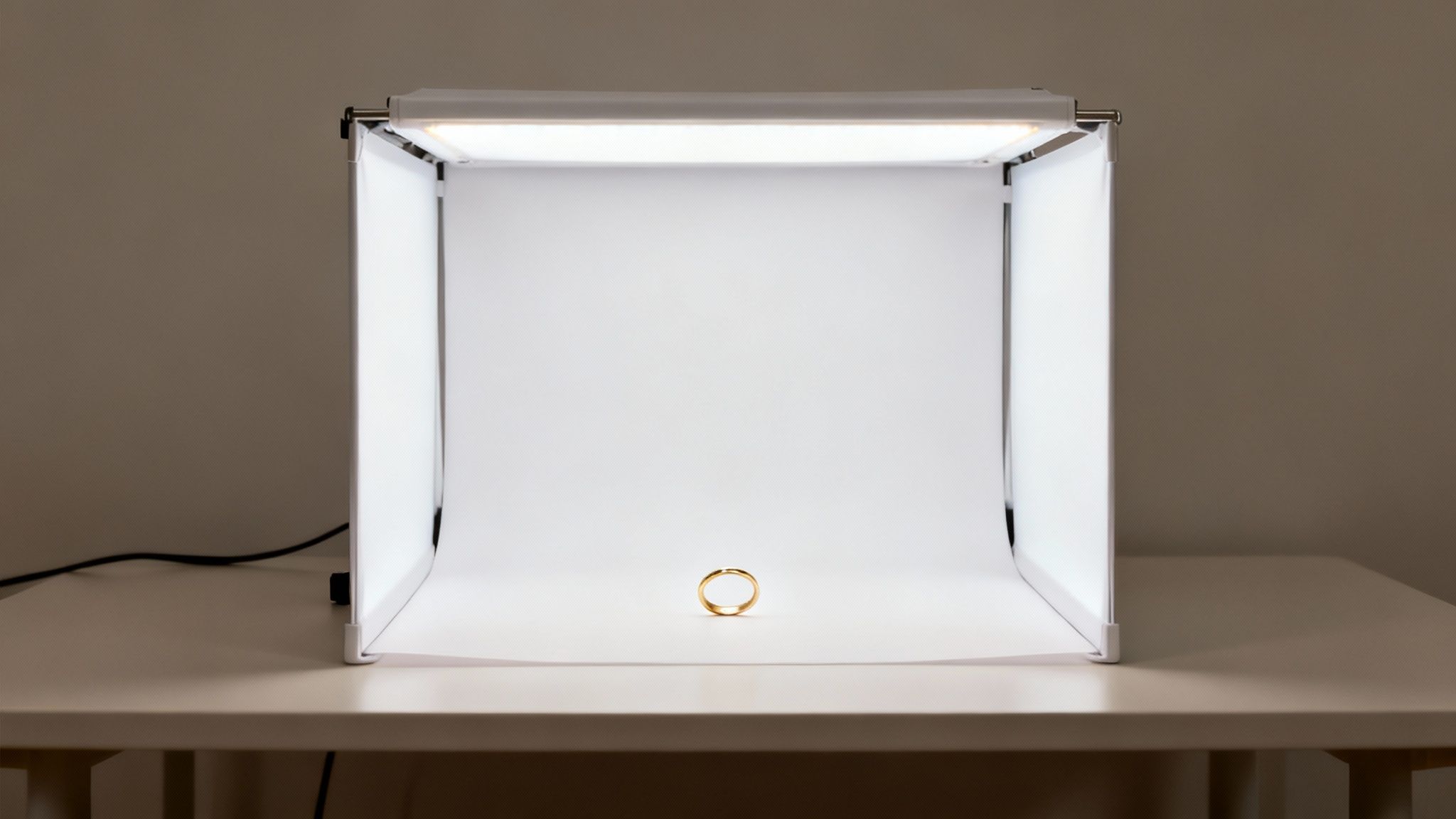 A simple gold wedding band standing inside a portable white LED light box for product photography.