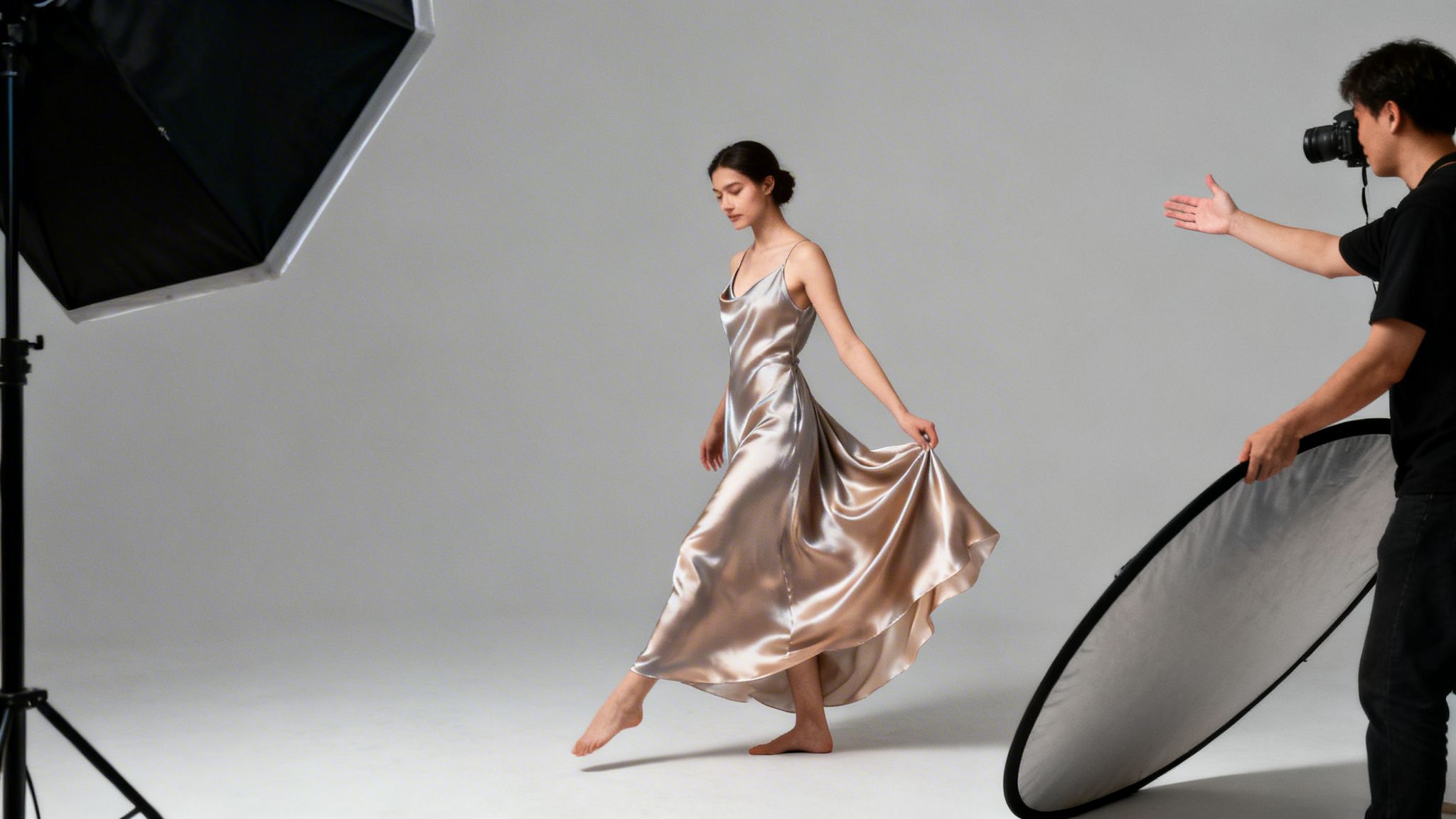 A woman in a silky dress poses during a professional studio photoshoot with a photographer and lighting.