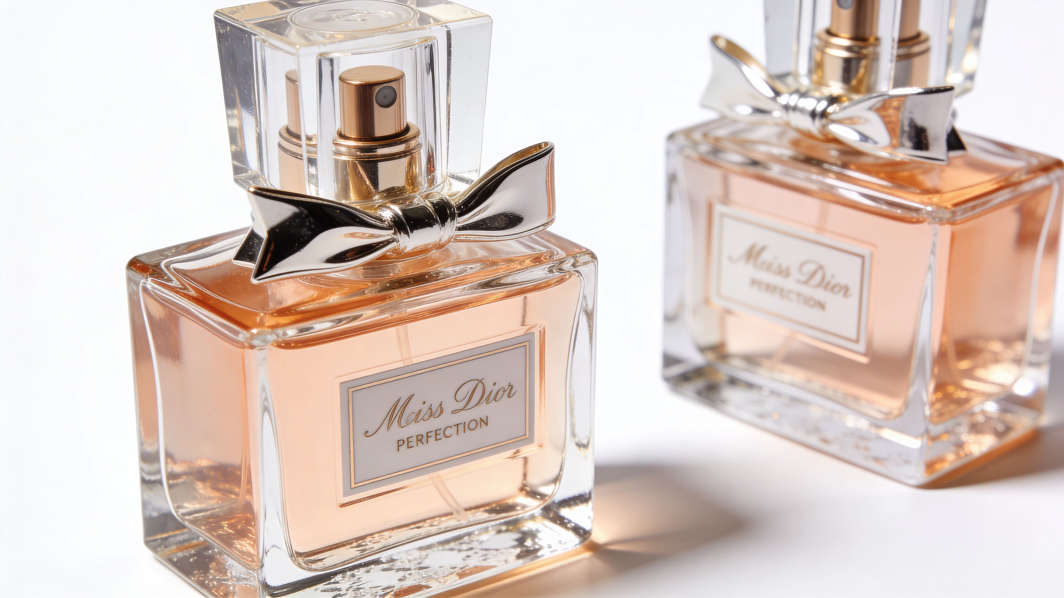 Two elegant bottles of Miss Dior Perfection perfume placed side by side against a clean white background.