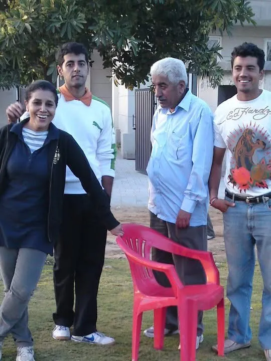 Three people standing outdoors behind a bicycle on grass with greenery in the background.