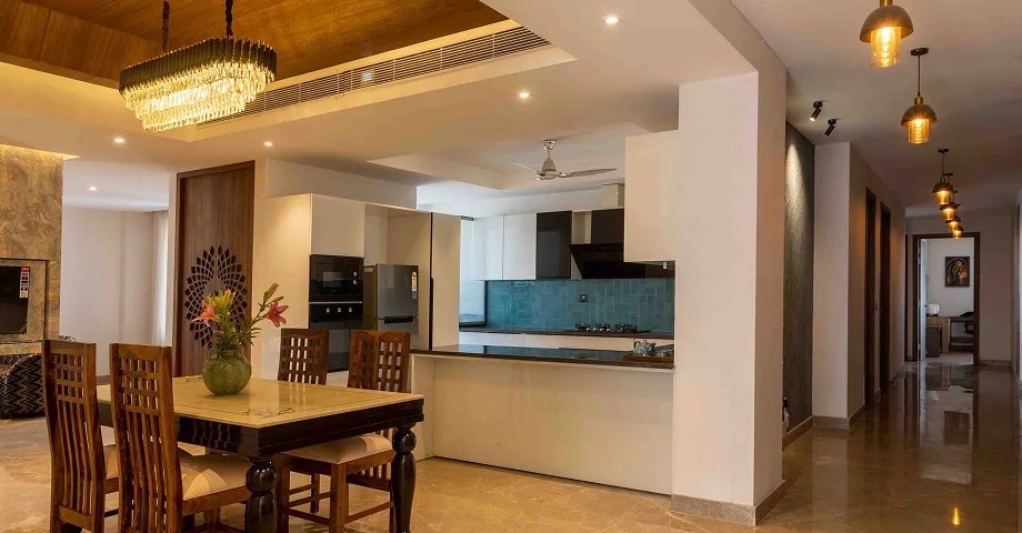 Spacious modern dining and living area in a serviced apartment with elegant lighting, wooden furniture, and an open kitchen.