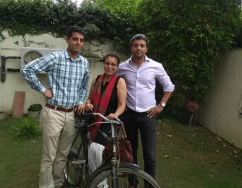 Three people standing outdoors with a bicycle; two men in casual shirts and trousers flank a woman wearing glasses and a red scarf.
