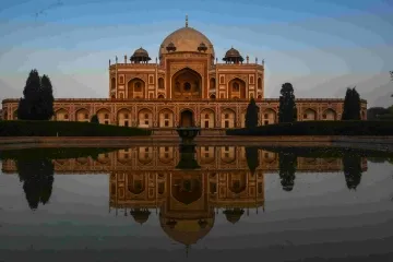 Humayun's Tomb with its reflection in a water pool under a clear blue sky.