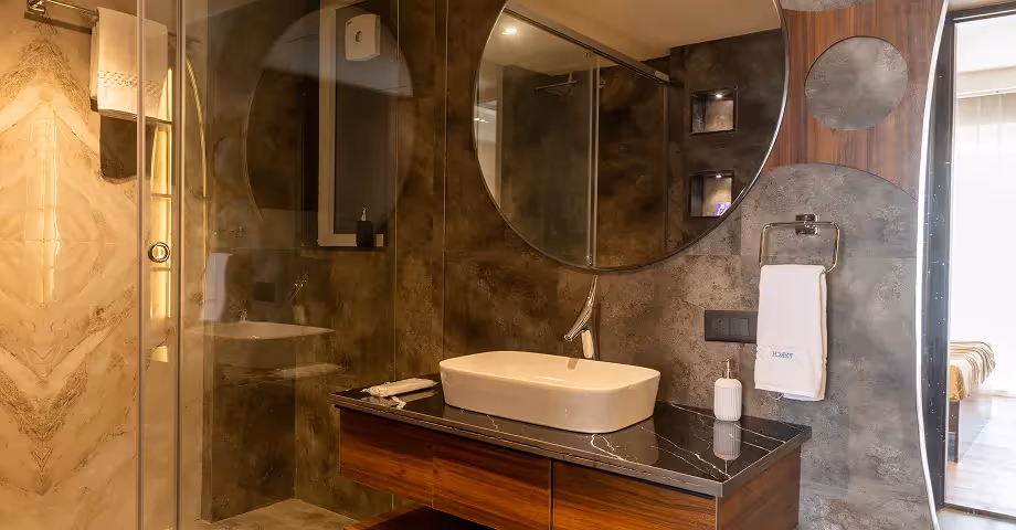 Elegant bathroom at 2BHK in Casa Feliz featuring warm lighting, a large round mirror, and premium sink fittings.