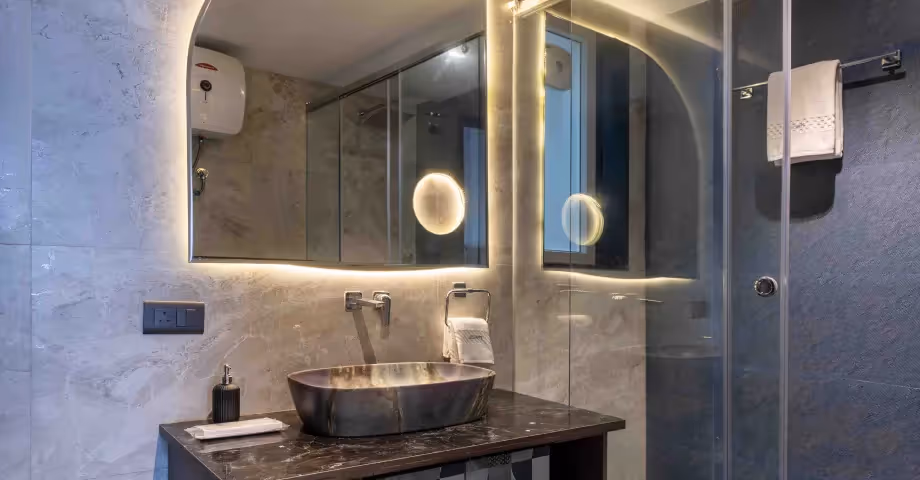Modern bathroom at 2BHK in Casa Feliz featuring a glass shower enclosure, round mirror, and elegant stone sink.