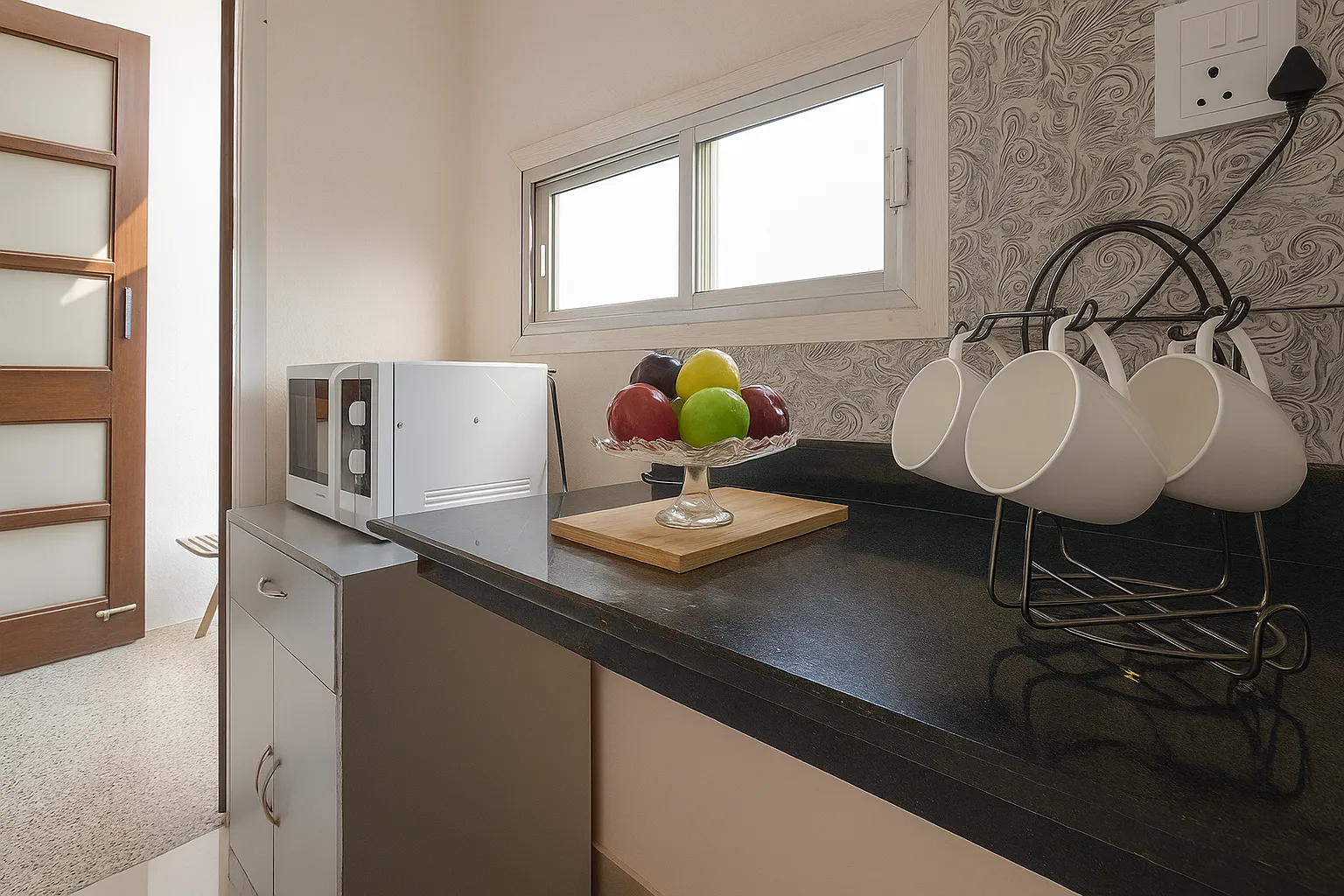 Compact kitchen at Sterling Studio Apartment in Sushant Lok featuring microwave, gas stove, sink, and essential cookware for a homely stay.