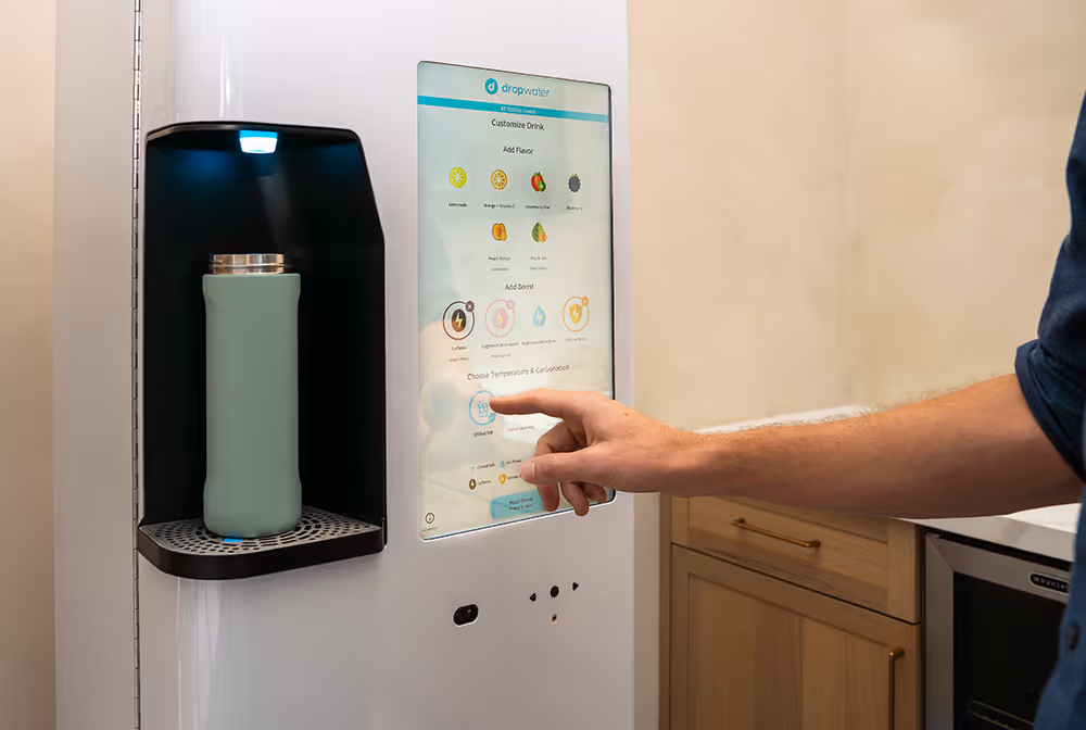 Person choosing drink options on touchscreen of a Dropwater beverage dispenser with a green bottle placed inside.