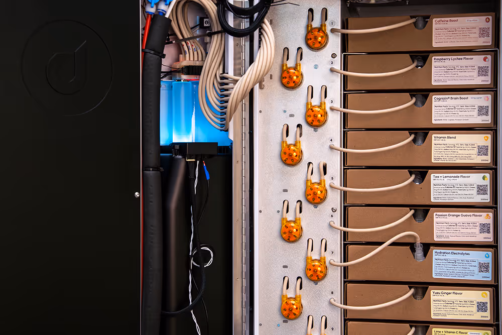 Interior view of a beverage dispenser machine showing labeled flavor cartridges connected with tubes.