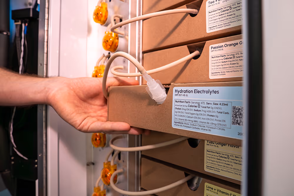 Hand retrieving a Hydration Electrolytes cardboard box connected to tubes inside a vending machine.