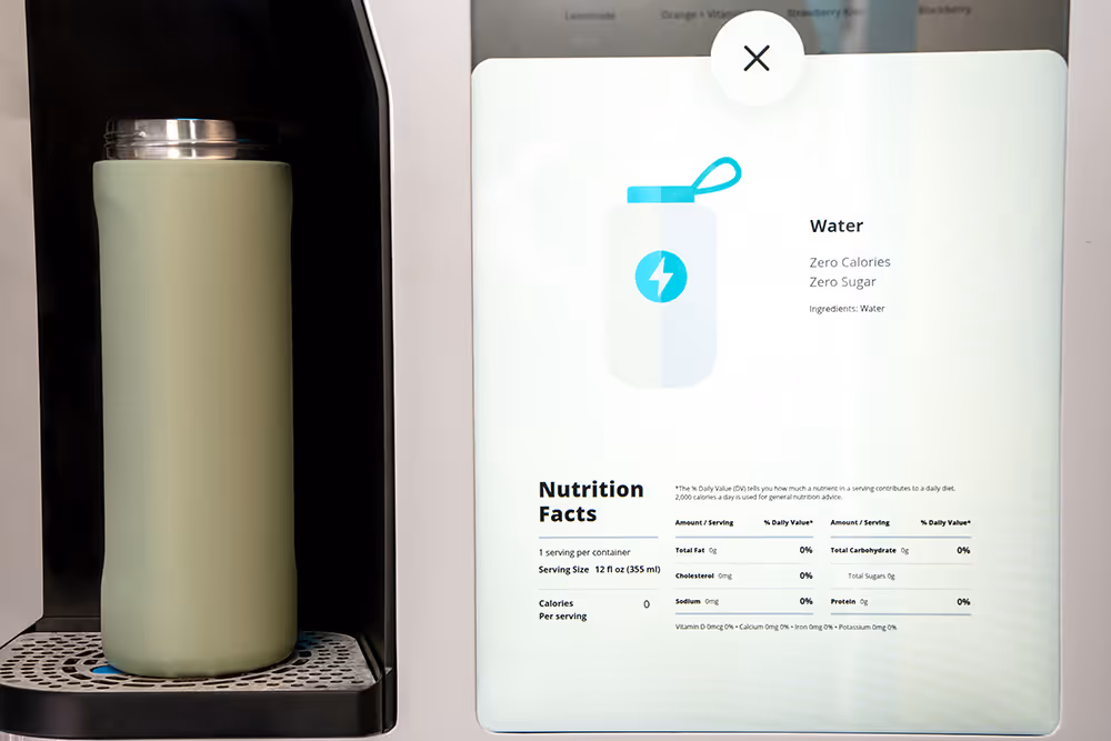 Touchscreen display showing nutrition facts for water with zero calories and zero sugar beside a green insulated water bottle on a dispenser.