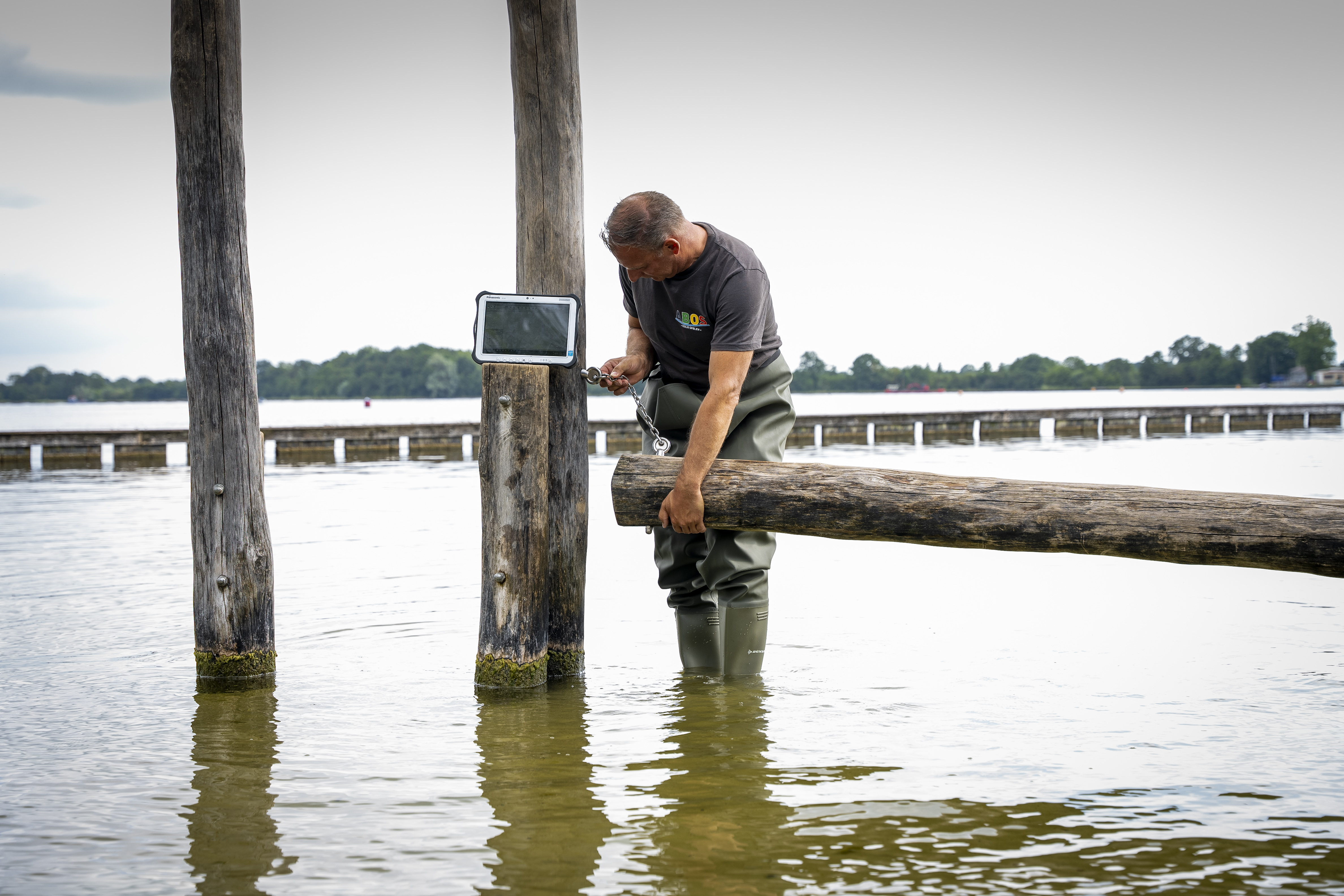 Een glimlachende ABOS-medewerker staat in het water met een waterbestendige overall en inspecteert een aansluiting
