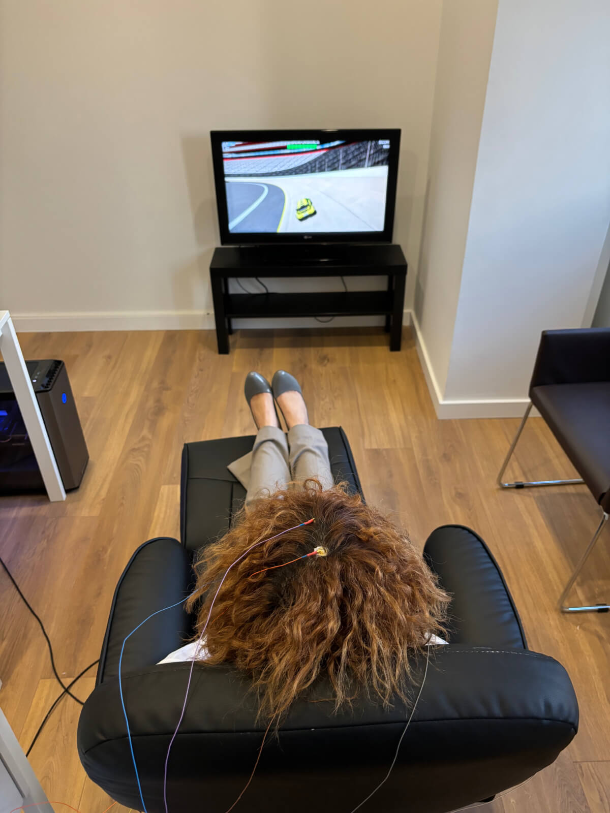 Mulher sentada em poltrona a fazer testes de neurofeedback enquanto vê televisão.