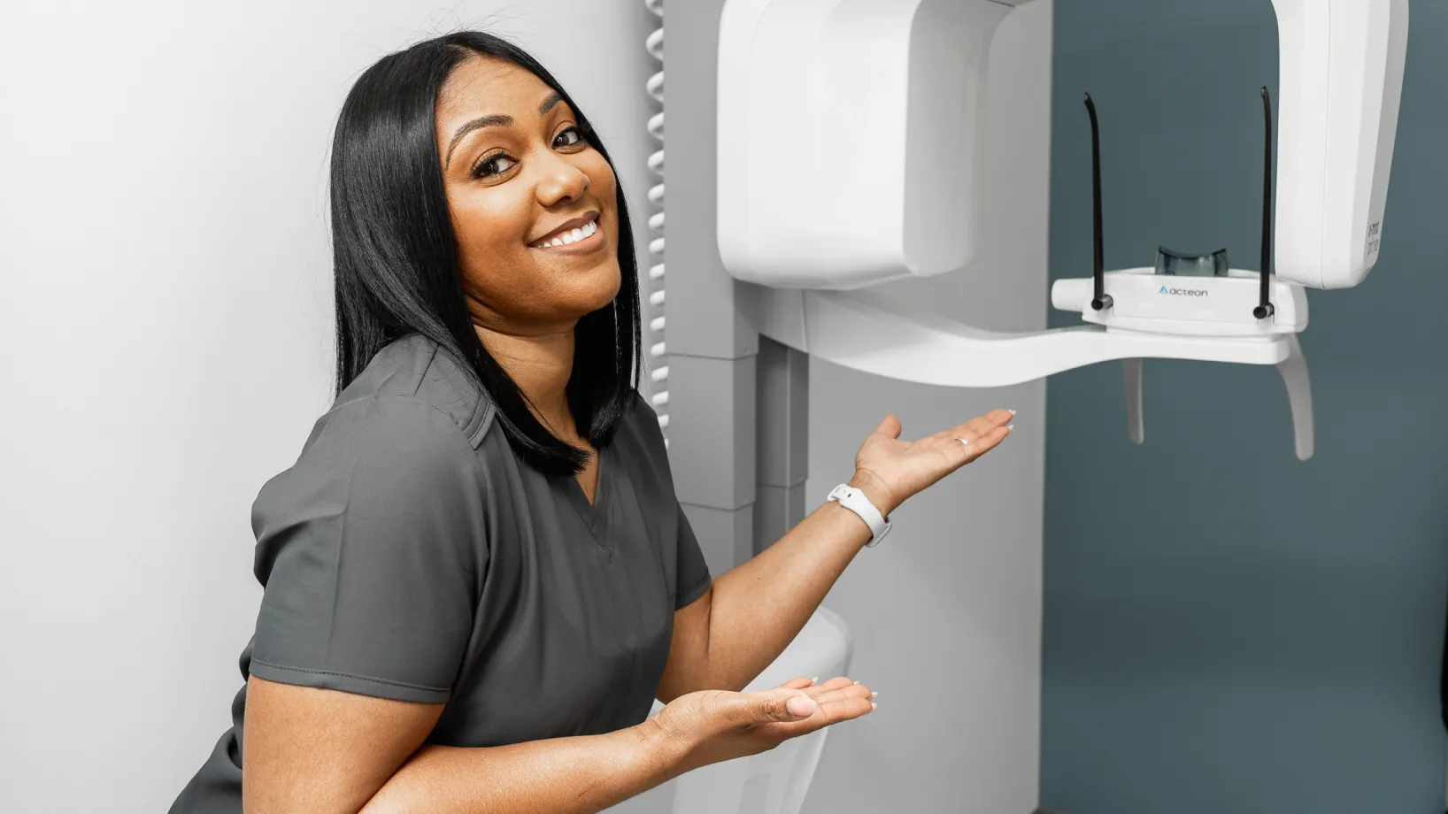 A woman standing next to a wall mounted toothbrush dispenser.
