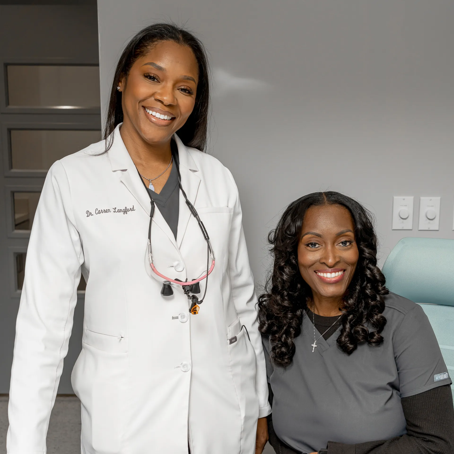 A woman in a white lab coat standing next to a woman in a gray shirt.