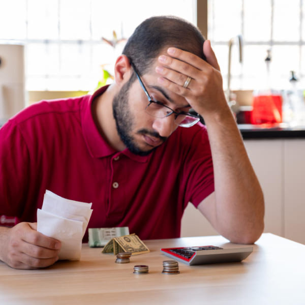 Homme préoccupé devant des factures, de la monnaie et une calculatrice, illustrant les causes fréquentes des problèmes financiers du quotidien.
