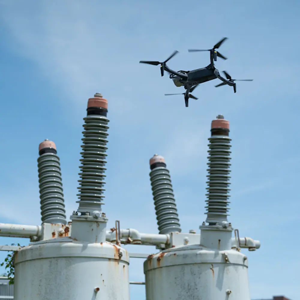 Skydio X10 drone flying above electrical substation equipment against a clear blue sky