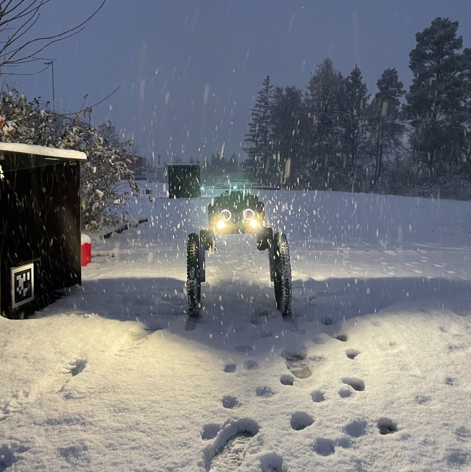 Autonomous security robot patrolling through heavy snowfall with headlights on.