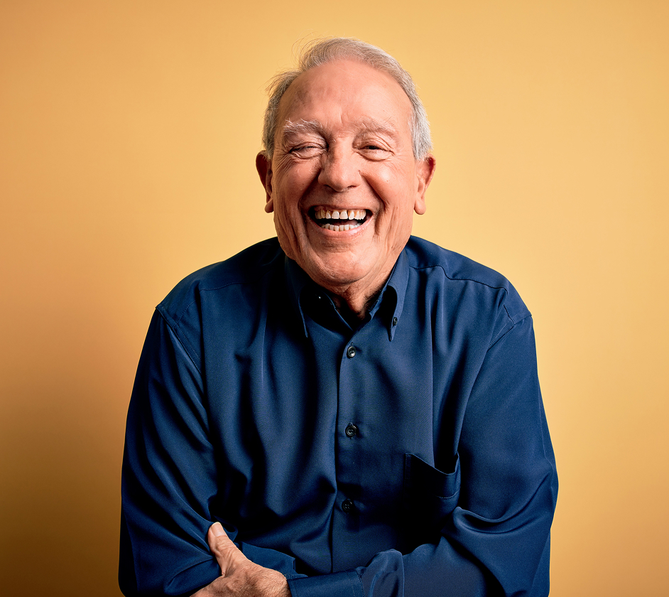 Older man with gray hair and a broad smile, promoting positivity and well-being for individuals with dementia, wearing a blue shirt against a yellow background.